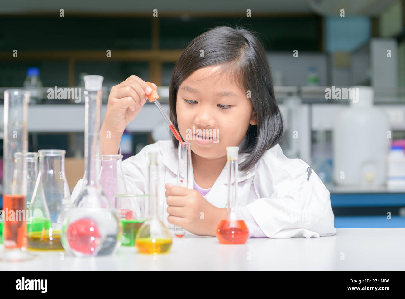 Happy little scientist in lab coat making experiment with test tube in ...