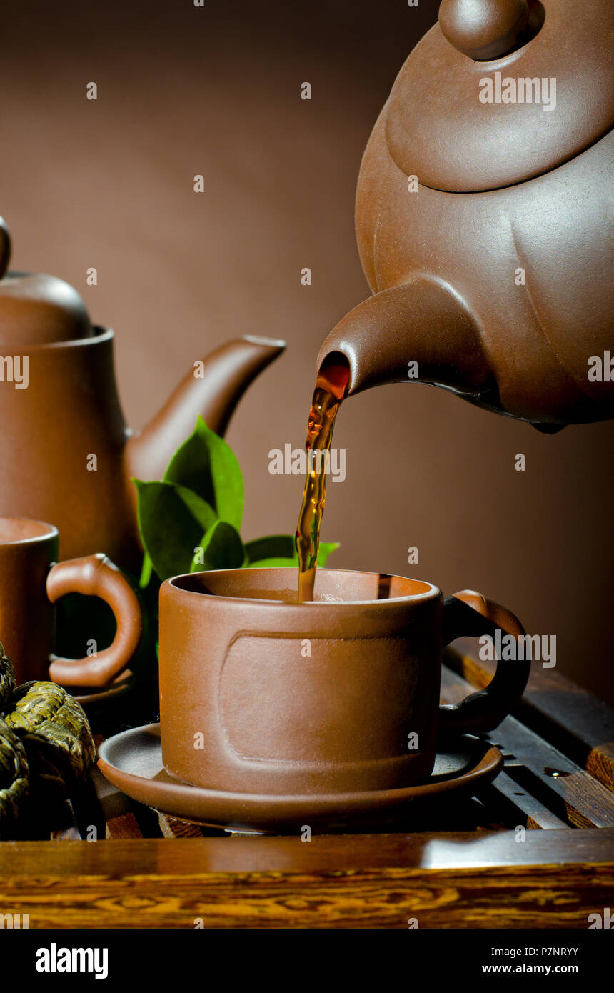 vertical photo, of the clay teapot tea flow in cup on brown background