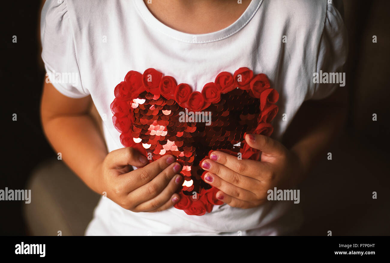 Conceptual composition, small girl holding a heart on her shirt. Stock Photo