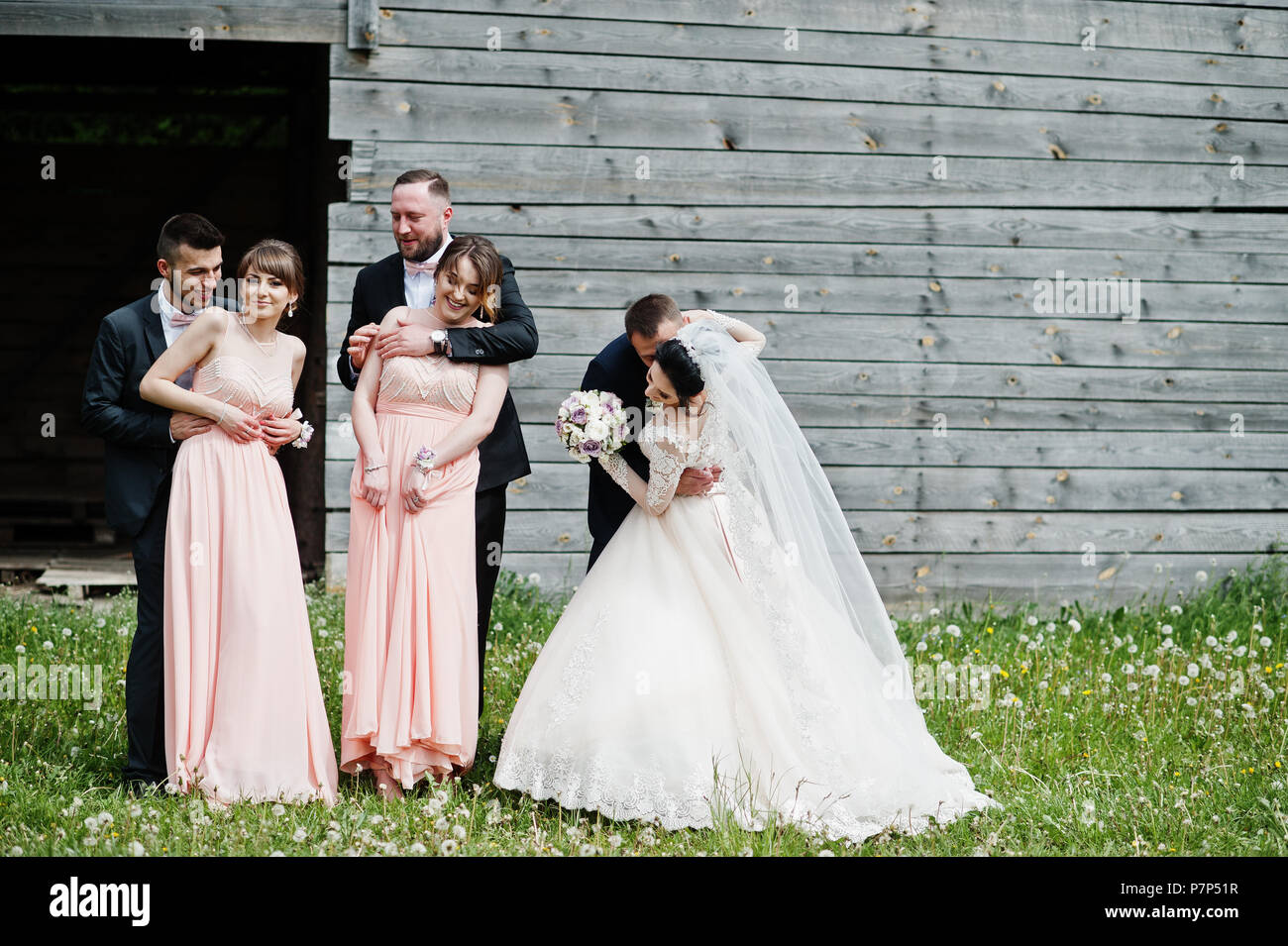 Bridesmaids with groomsmen and wedding couple having fun outdoors next to the old rustic wooden barn. Stock Photo