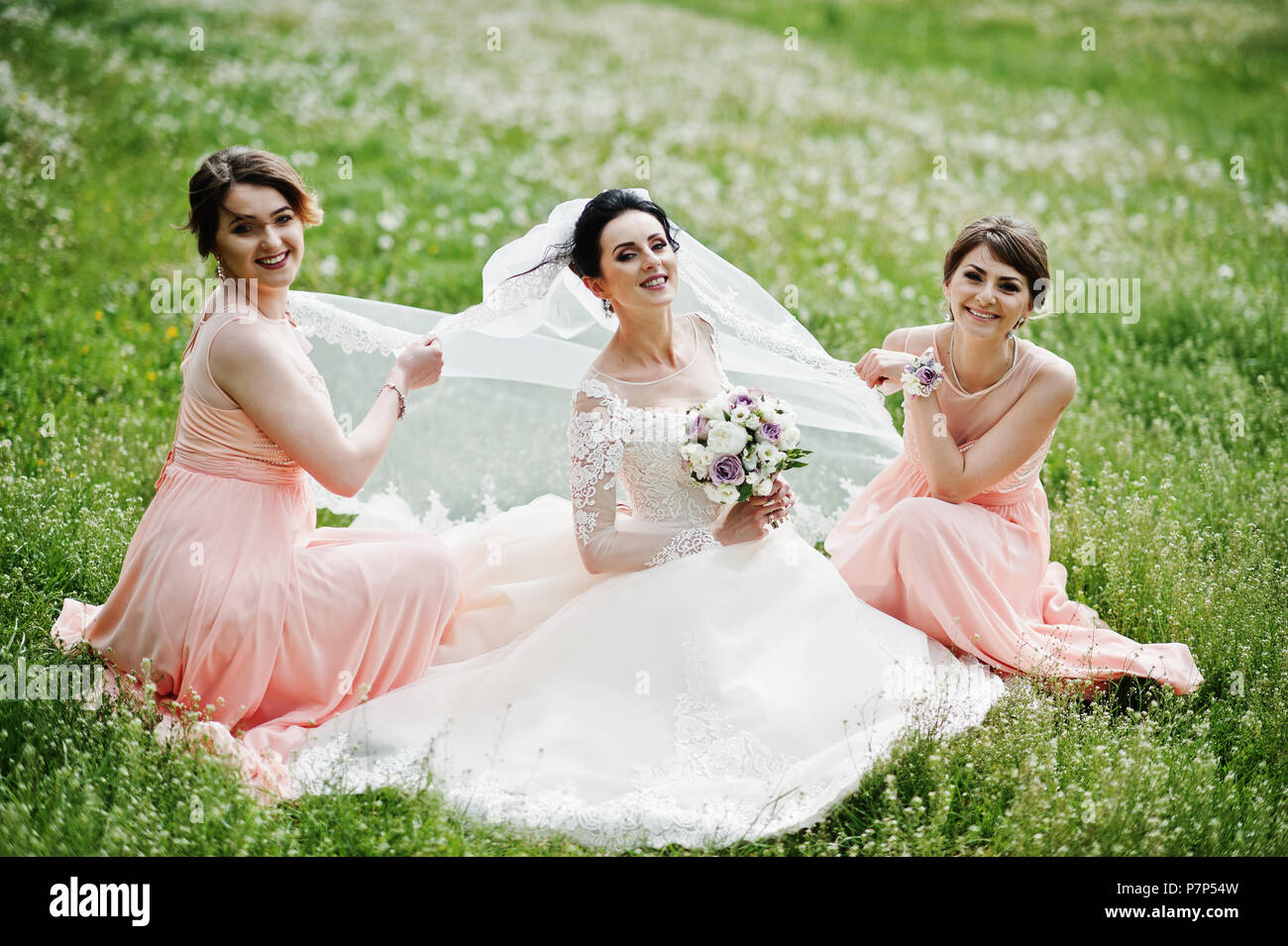 beautiful bride sitting and posing with bridesmaids on the field full of flowers on the wedding day P7P54W