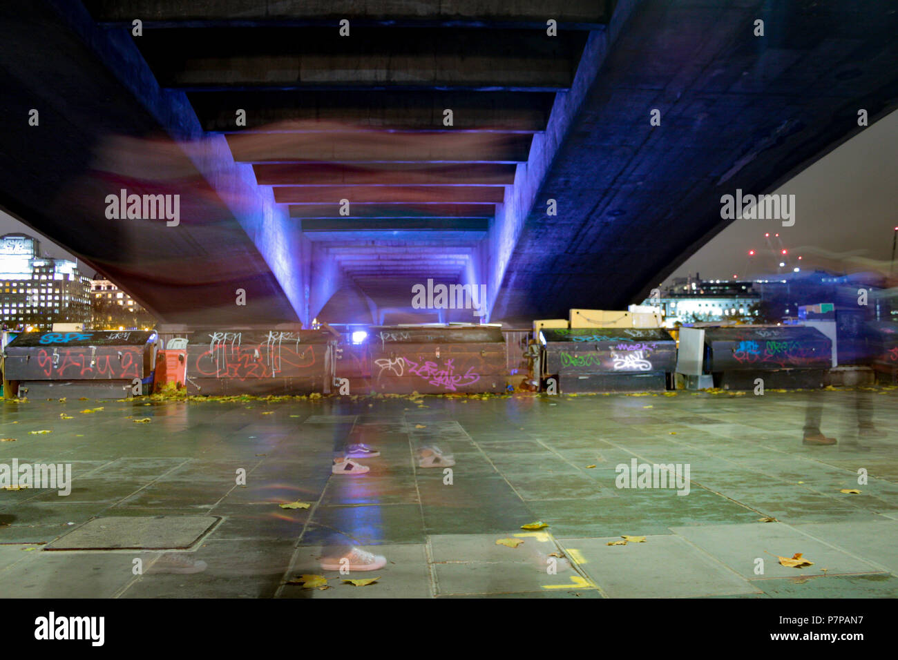 Underside of a graffiti covered concrete bridge - South Bank of the Thames, London. Long exposure with blurred feet adding movement to the image. Stock Photo