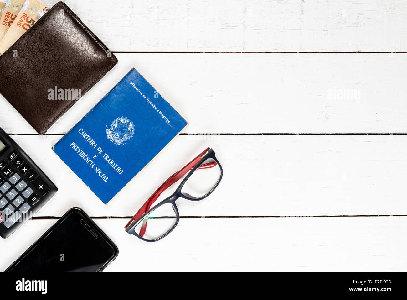 work permit, wallet,  Brazilian money, caclulator, glasses, cellphone, white background, space for text, pinus background, objects on the left, top vi Stock Photo