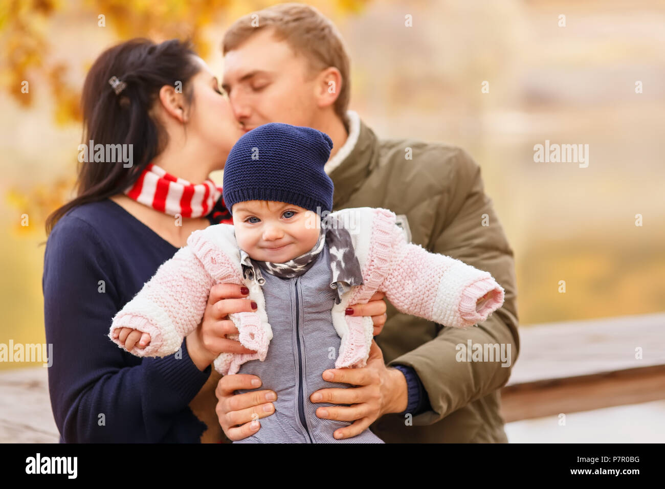 young parents with little daughter in autumn forest. Mom and dad holding baby girl in hands. Happy family concept Stock Photo
