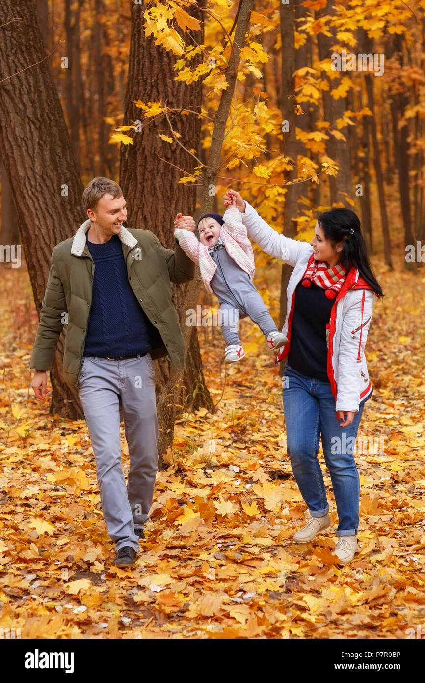 young parents walk and play with little daughter in autumn park. Dad and mom holding baby girl. Happy family concept Stock Photo