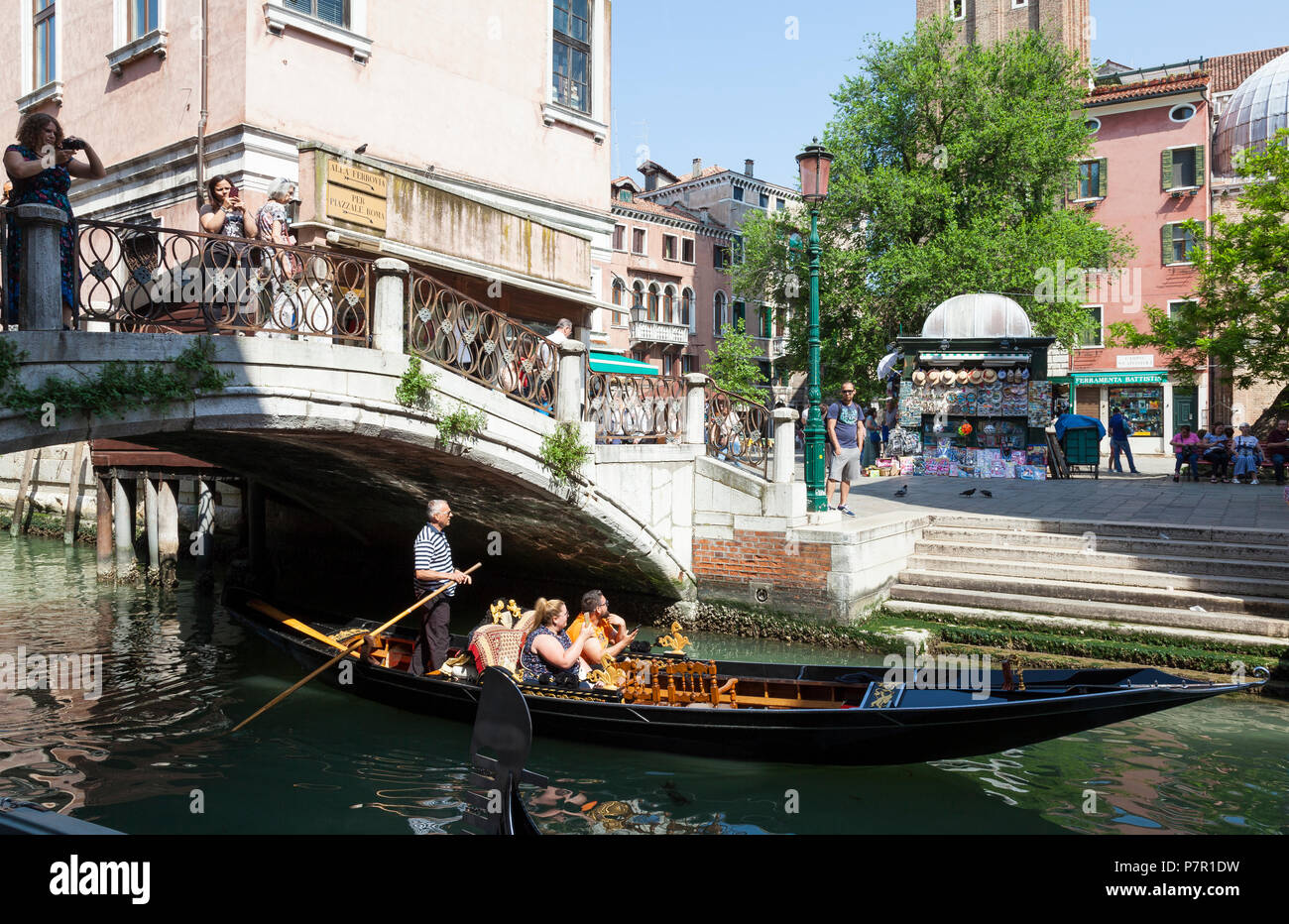 Gondolier rowing tourists through Cannaregio, Venice, Veneto, italy in his sandolo, passing Campo Santi Apostoli under  a bridge Stock Photo