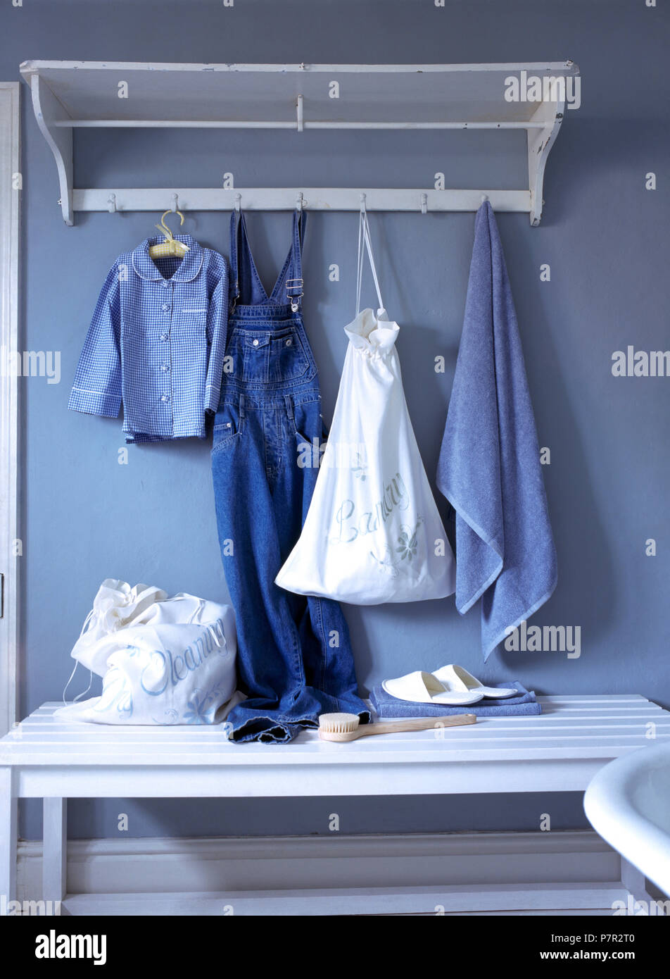 Children's clothes and hand made linen laundry bag on hooks on a painted wooden shelf Stock Photo