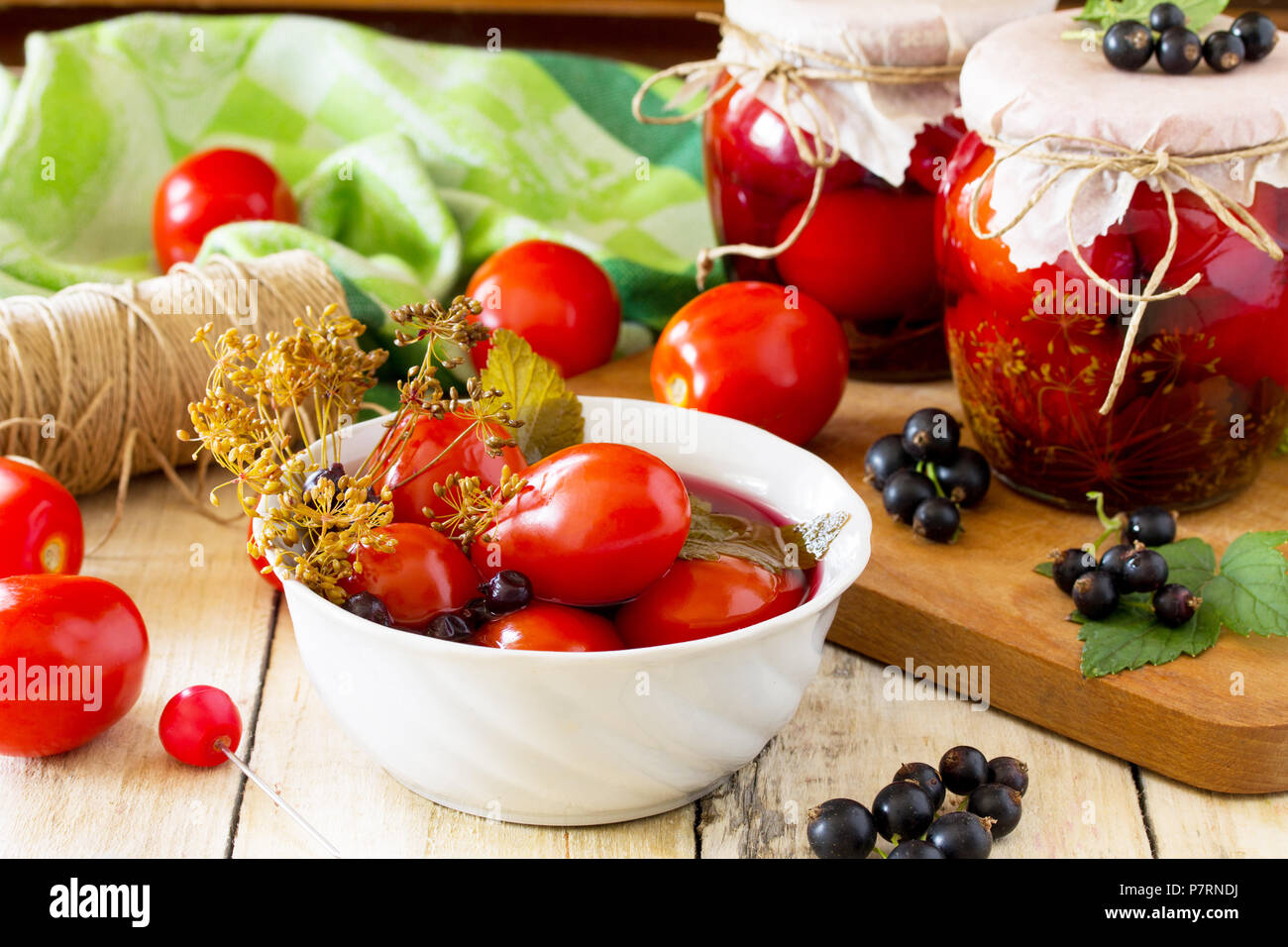 Marinated tomatoes. Pickles tomatoes with black currant on the kitchen table in a rustic style. Stock Photo