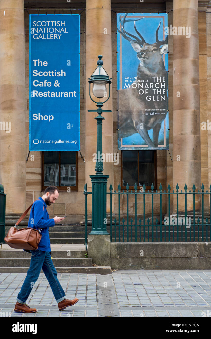 A visitor walking by the entrance to the National Gallery of Scotland at the Mound in Edinburgh with an advert out front for the Monarch Of The Glen. Stock Photo