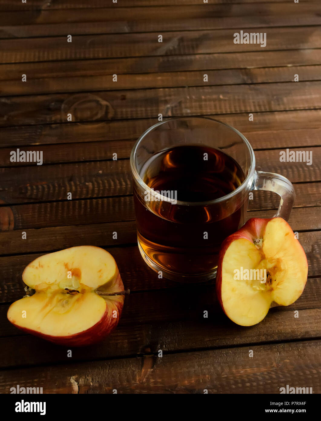 The glass of apple cider vinegar and two red halves of the apple on wooden background. Two red halves of the apple darkens on the cut..Copyspace top.V Stock Photo