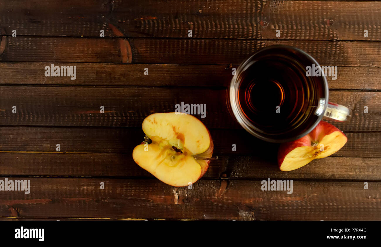 The glass of apple cider vinegar and two red halves of the apple on wooden background. Two red halves of the apple darkens on the cut. Flat lay view.C Stock Photo