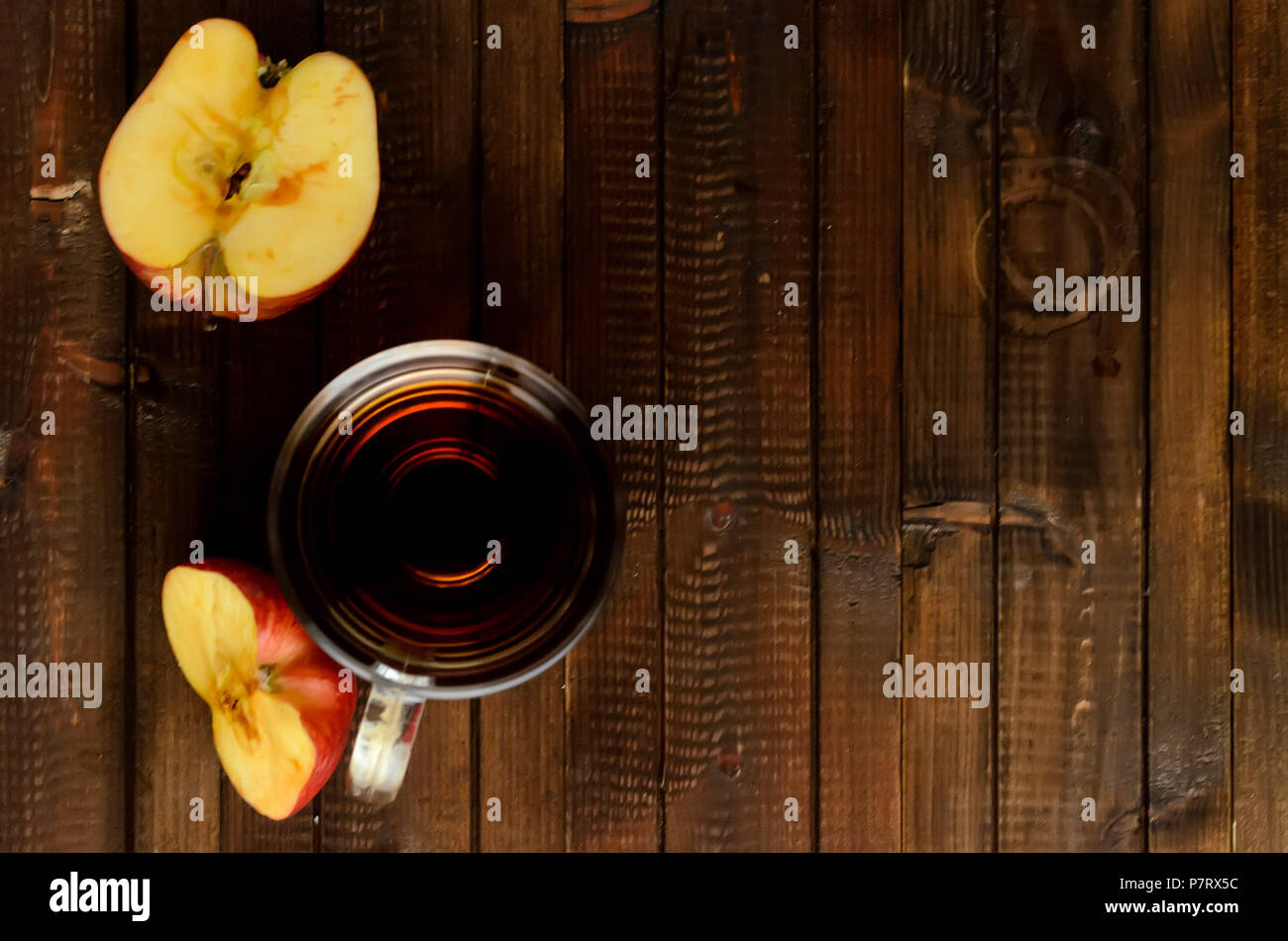 The glass of apple cider vinegar and two red halves of the apple on wooden background. Two red halves of the apple darkens on the cut. Flat lay view.C Stock Photo