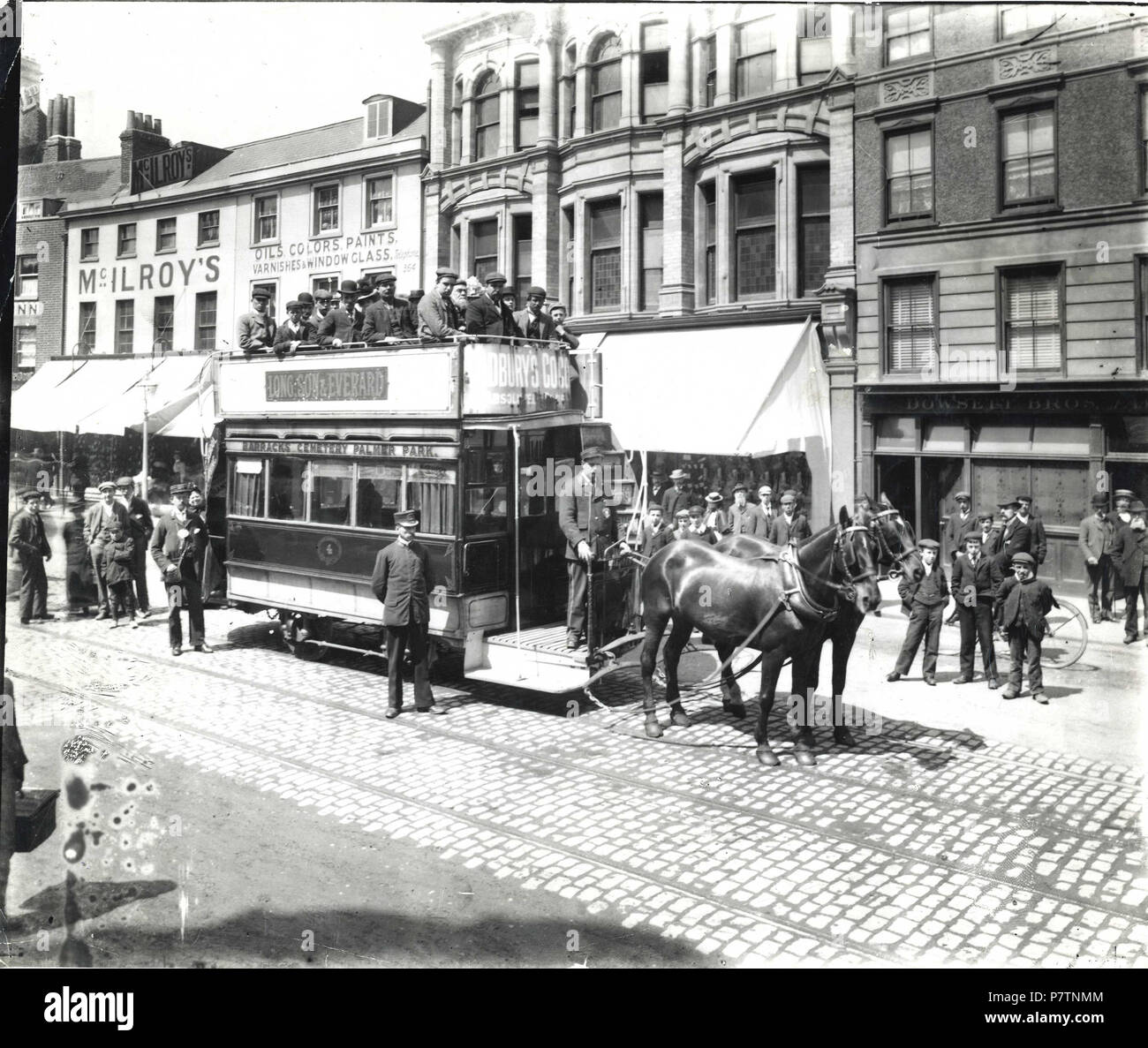 English: Reading Tramways Company. Horse-tram No. 4 in Broad Street, c. 1900, heading eastwards on the 'Barracks - Cemetery - Palmer Park' route. The driver, conductor and inspector pose for the camera. The saloon is almost empty, but the upper deck is thronged, and there are several spectators in the picture. Recognisable shops in the background: No. 50 (William McIlroy, boot and shoe warehouse); No. 49 (William Archer oils, colours, paints and varnishes); Nos. 47 amd 48 (A. H. Bull, gentlemen's and boys' outfitters); No. 46 (Dowsett Brothers, brewers). 1900-1909 : photograph by Walton Adams. Stock Photo
