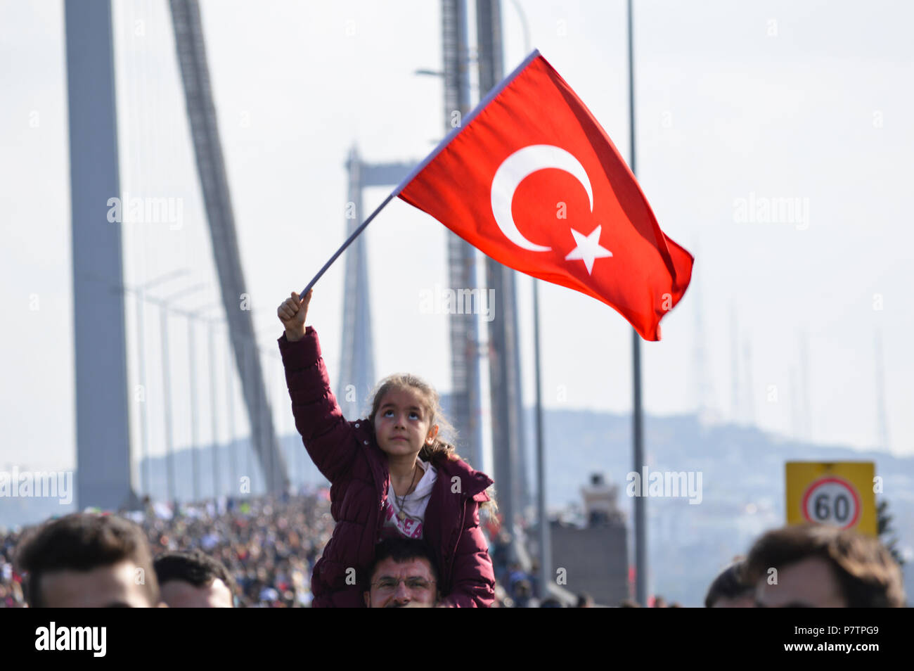 Istanbul, Turkey - November 15, 2015 :Girl holding Turkish flag while Turkish people cross 15 Temmuz Demokrasi ve Sehitler Koprusu (Bosphorus Bridge). Stock Photo