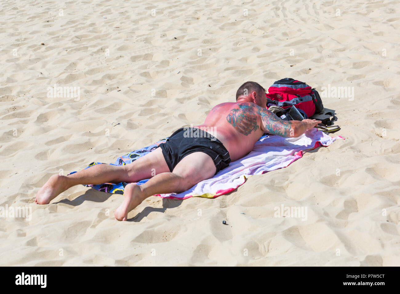 Bournemouth, Dorset, UK. 8th July 2018. UK weather: another hot sunny day as the heatwave continues and thousands of sunseekers head to the  seaside to enjoy the sandy beaches at Bournemouth on the South Coast. A bit red - looks sore! Man with colourful tattoos tattoo on back and arm sunbathing on the beach getting sunburnt. Credit: Carolyn Jenkins/Alamy Live News Stock Photo