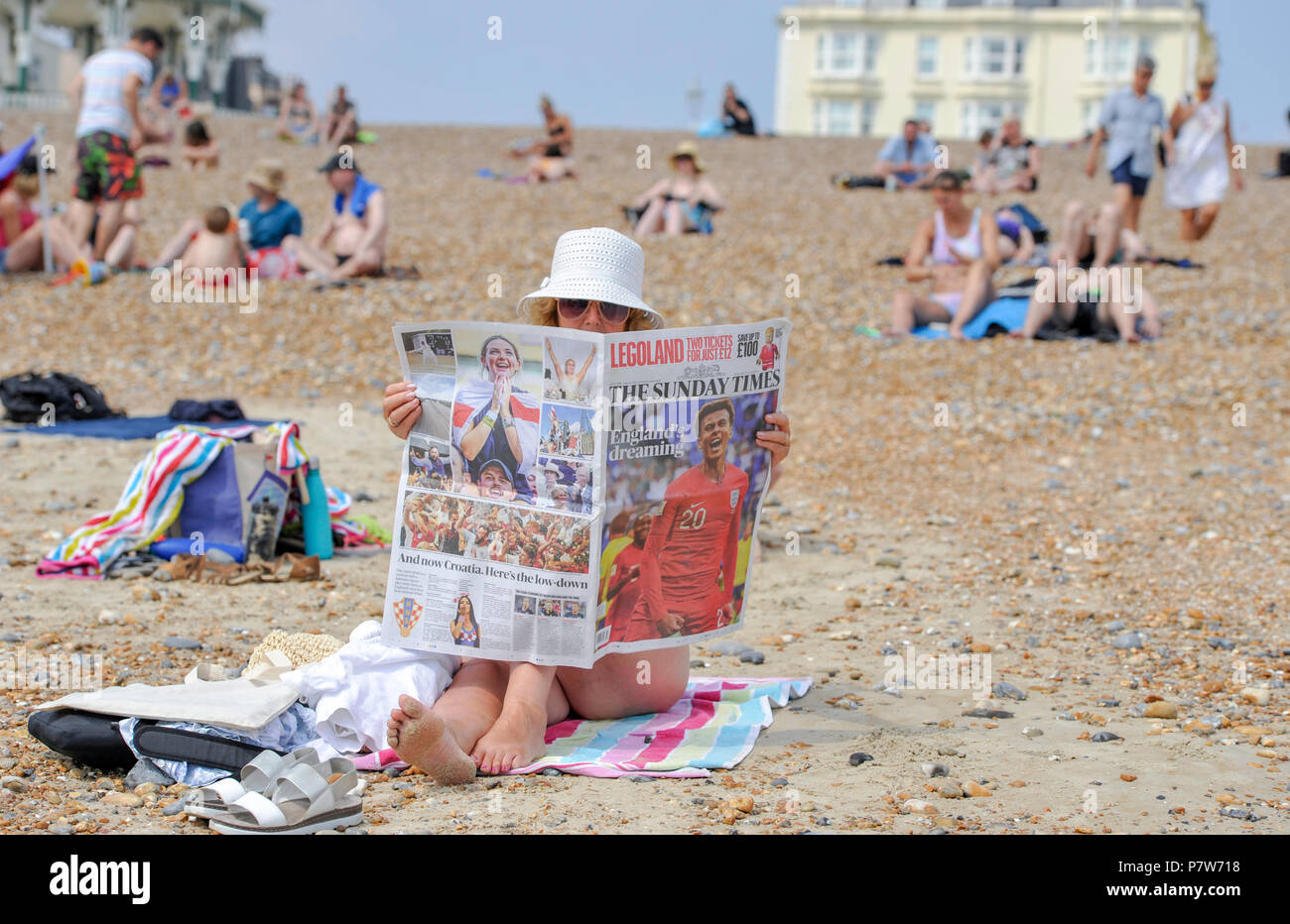 Brighton UK 8th July 2018  - A woman reads the Sunday Times newspaper about yesterdays England win in the World Cup on Brighton beach as the heatwave continues throughout Britain Credit: Simon Dack/Alamy Live News Stock Photo