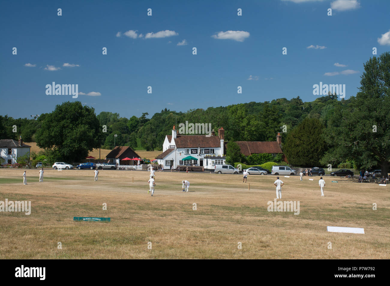 Tilford, Surrey, UK. 8th July, 2018. As the heatwave continues, people were having fun in the sun on a beautiful Sunday afternoon in the pretty village of Tilford. Many were cooling off in the river or sunbathing, while a cricket match was being played on the village green. Stock Photo