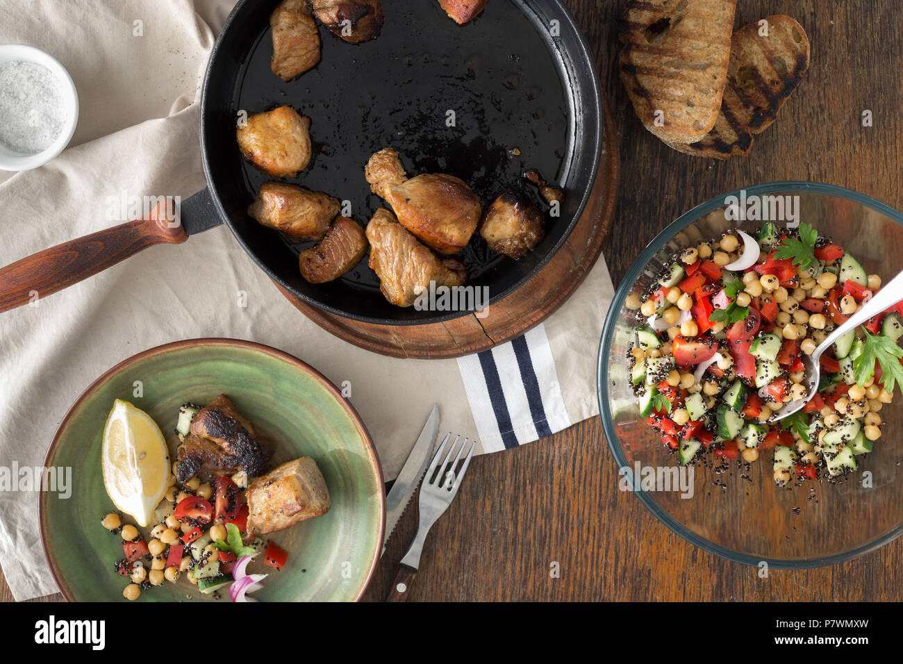 Fried meat in pan on wooden table with fresh vegetable salad of black quinoa and chickpeas, top view. Simple and healthy homemade food Stock Photo