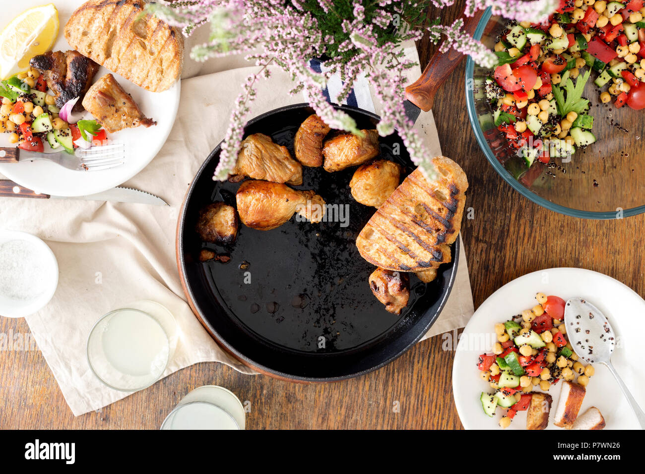 Pieces fried in pan on wooden table with fresh vegetable salad of black quinoa and chickpeas and glass of lemonade, top view. Tasty dinner table conce Stock Photo