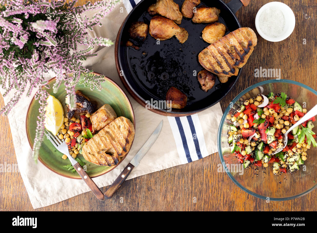 Pieces roast meat in pan on wooden table with fresh vegetable salad of black quinoa and chickpeas, top view. Healthy homemade food Stock Photo