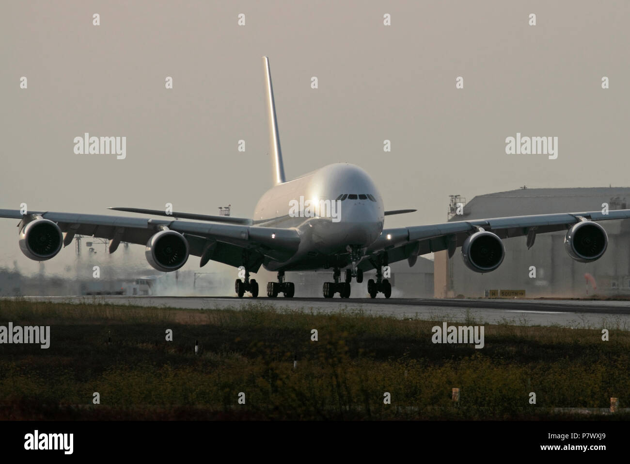 Airbus A380 four-engine long haul passenger jet airplane landing on runway with tyre smoke on touchdown. No livery or proprietary details visible Stock Photo