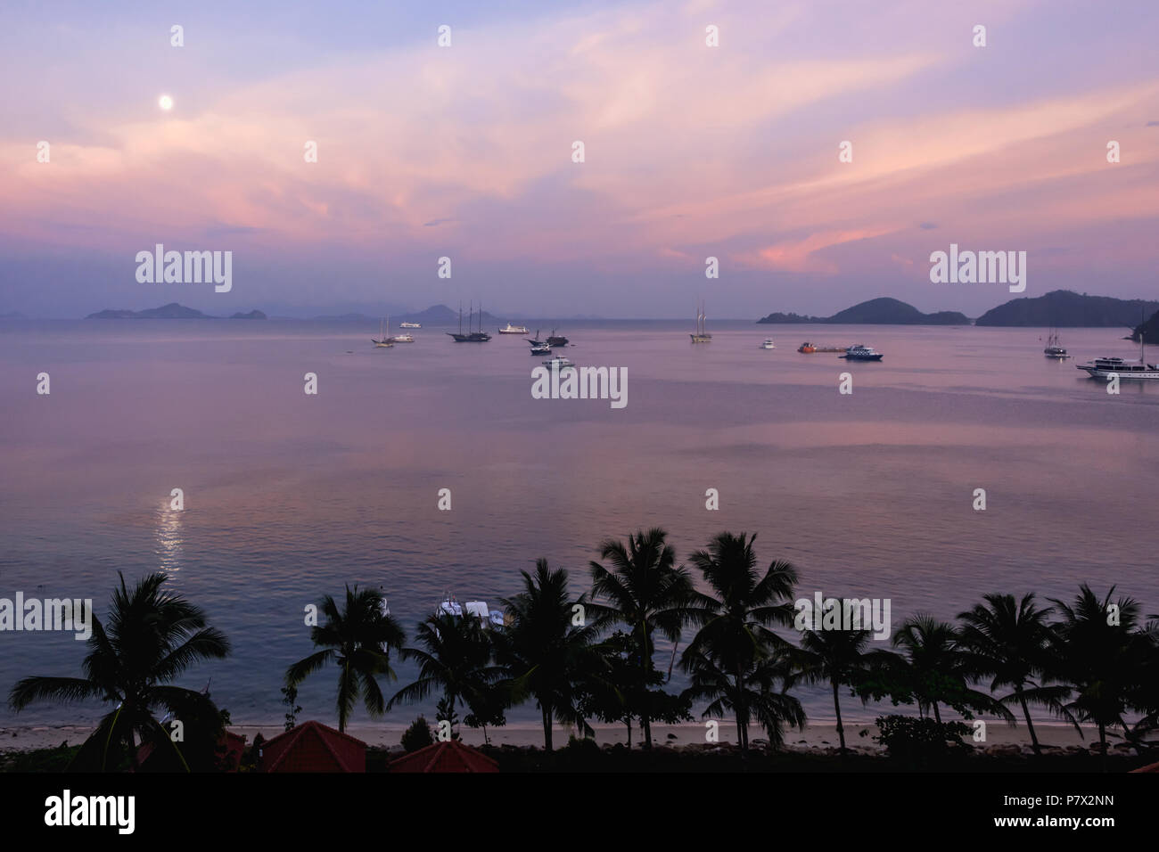 Sunrise with full moon and boats, Labuhan Bajo Harbour, East Nusa Tenggara, Indonesia Stock Photo