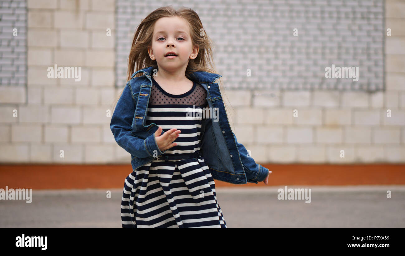 Little girl in striped dress and a denim jacket runs forward. Long hair ...