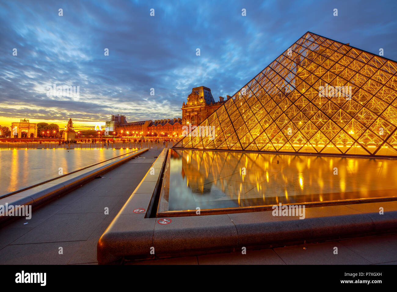 Paris, France - July 1, 2017: wide angle view of glass Pyramid and Pavillon Rishelieu reflecting at twilight. Cour Napoleon at blue hour. Cultural art picture gallery hosting Gioconda of Leonardo. Stock Photo