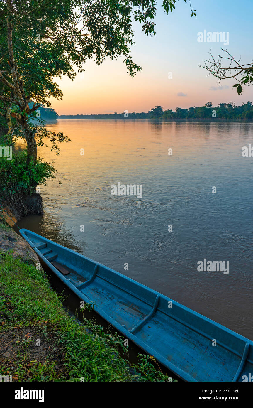 Vertical photograph of a turquoise canoe at sunset along the Napo river inside the Yasuni national park, Ecuador. Stock Photo