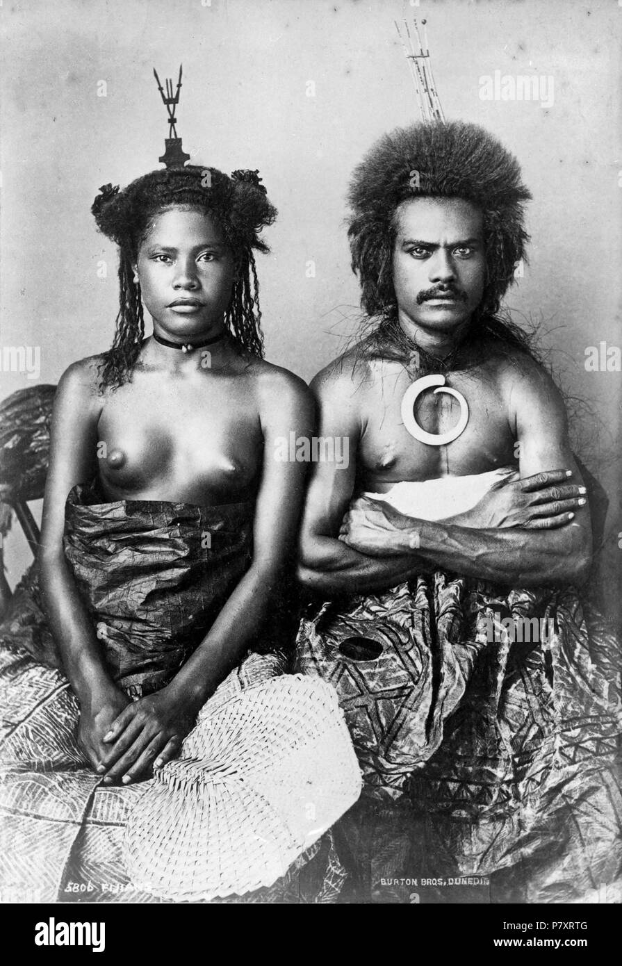 English: Seated portrait of a Fijian man and a Fijian woman. Both wear headpieces. Tapa cloths are draped over their legs. Photograph taken by Alfred Burton in 1884. 1884 159 Fijian man and woman, 1884 Stock Photo
