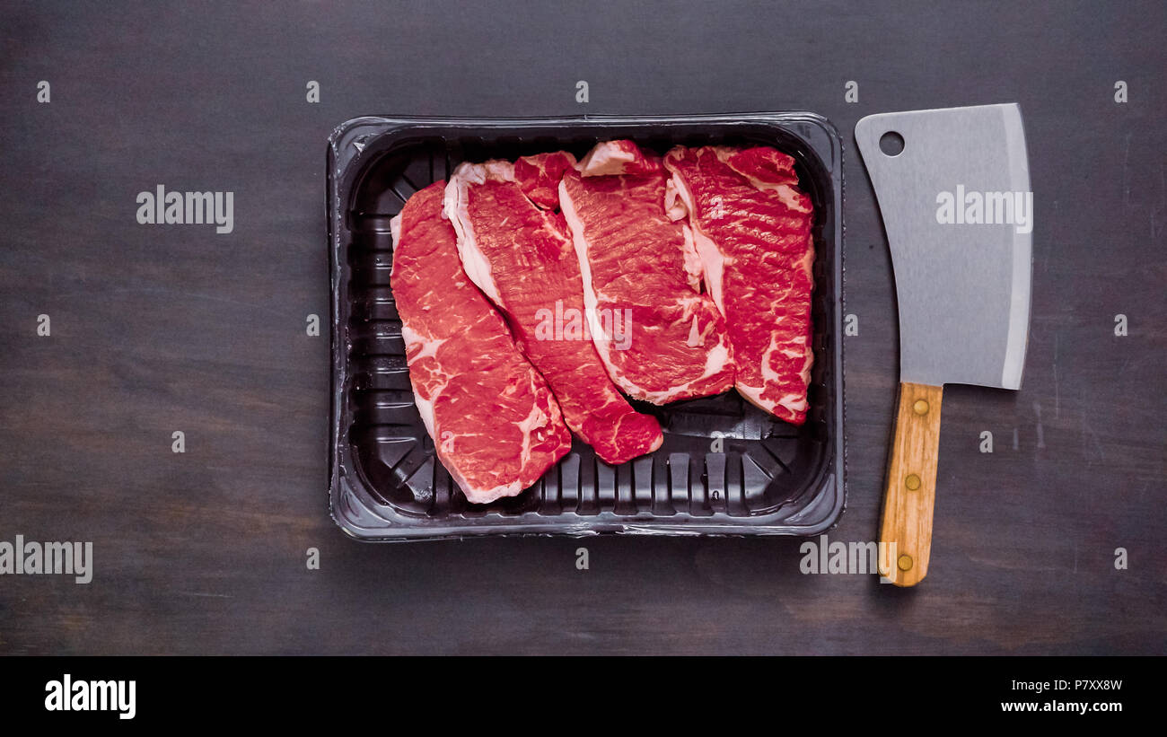 Raw New York strip steaks in black plastic meat packaging container ...
