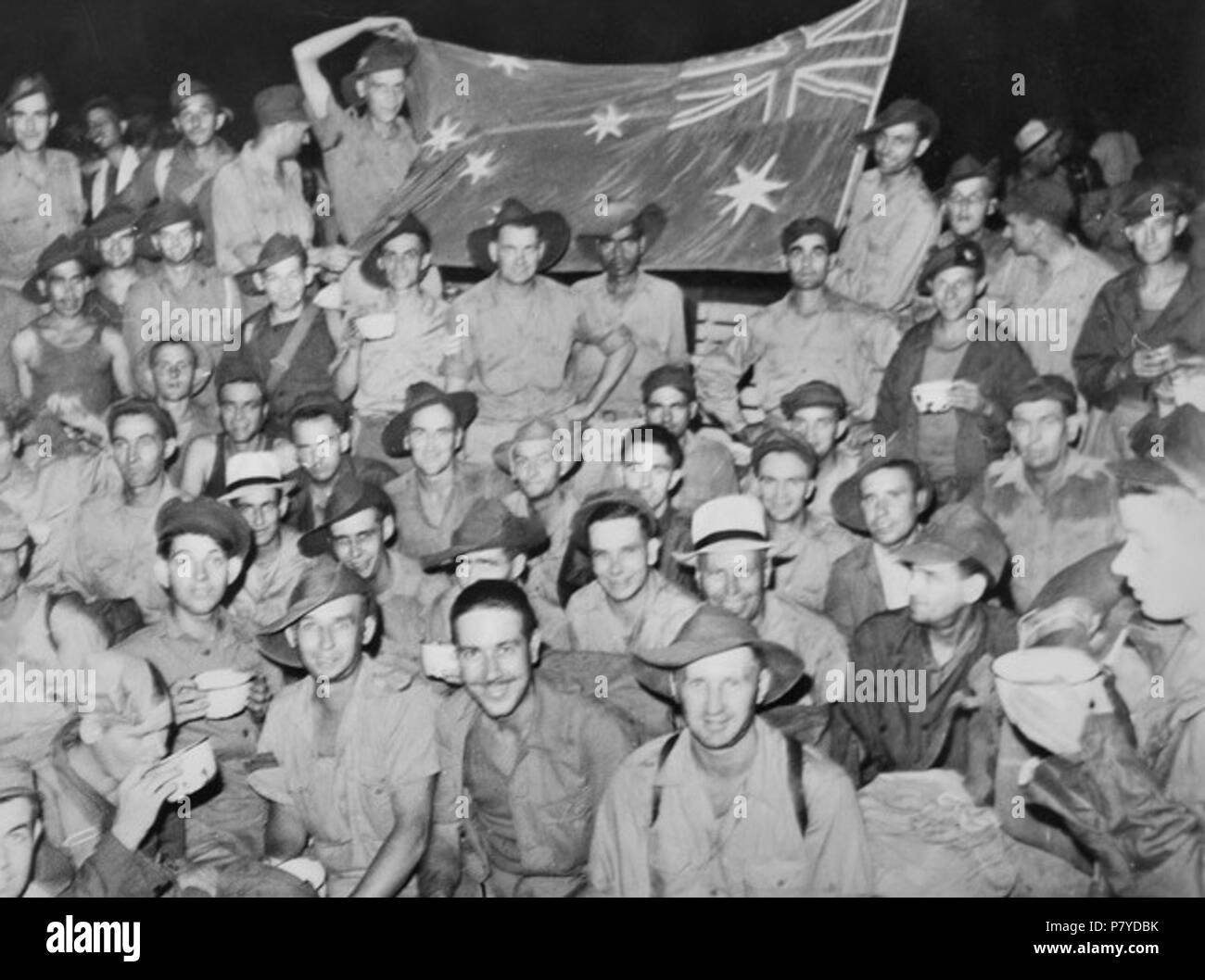 English: According to the Australian War Memorial the caption to this photograph reads: 'Yokohama, Japan. September 1945. These Australian men smiling and displaying the Australian flag they are so proud of were amongst 231 prisoners of war (POWs) released and brought into Yokohama in the middle of the night. The lateness of the hour did not stop them from demonstrating their joy at release. The flag was made and sown by hand from pieces of coloured parachutes used to drop supplies to them while still in camp. All these men were members of 8th Division. They were captured in Singapore and Mala Stock Photo