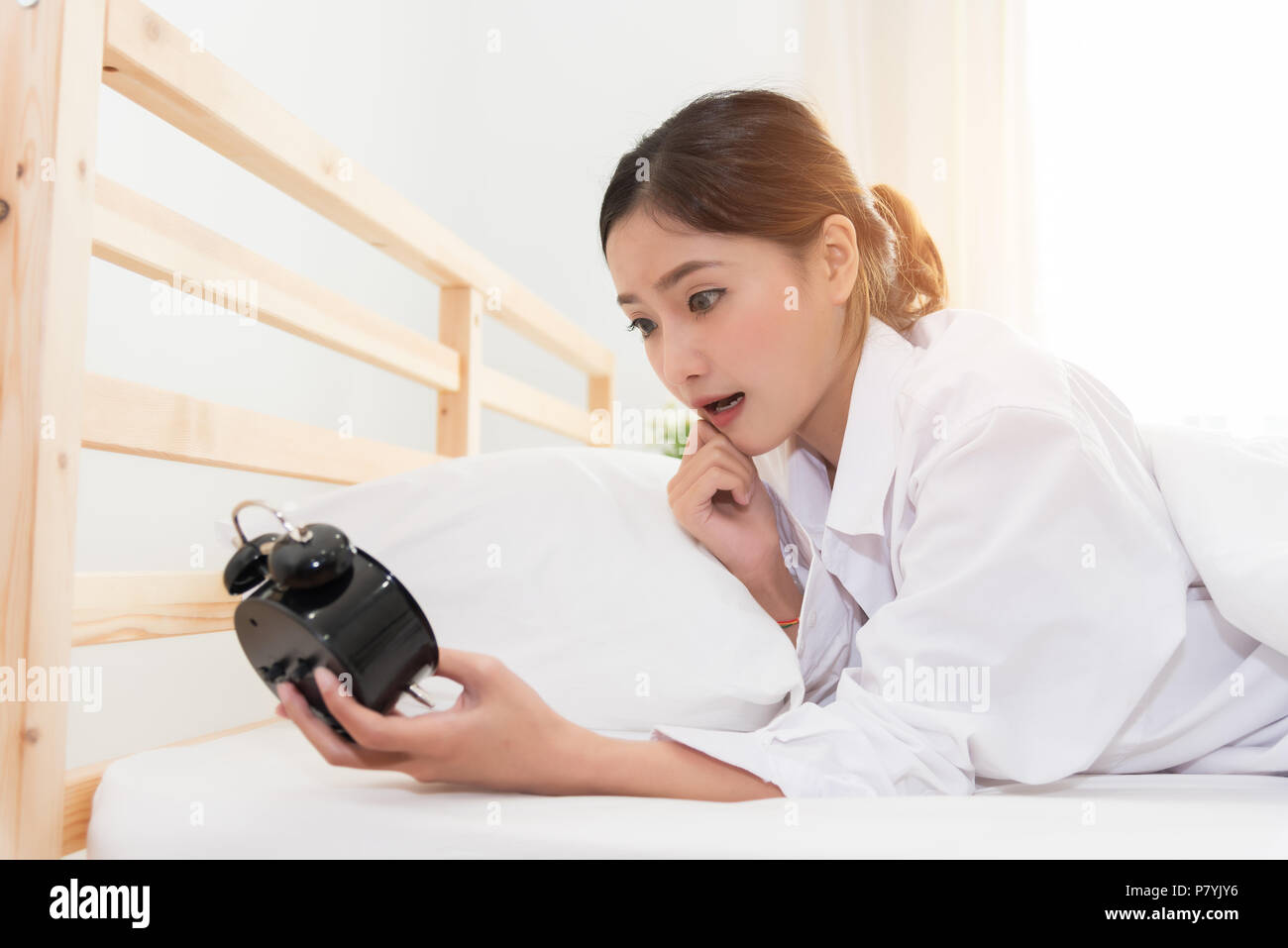 Asian woman shocked when wake up by alarm clock because too late for meeting appointment or working. Lazy day and Hurry up concept. Stock Photo