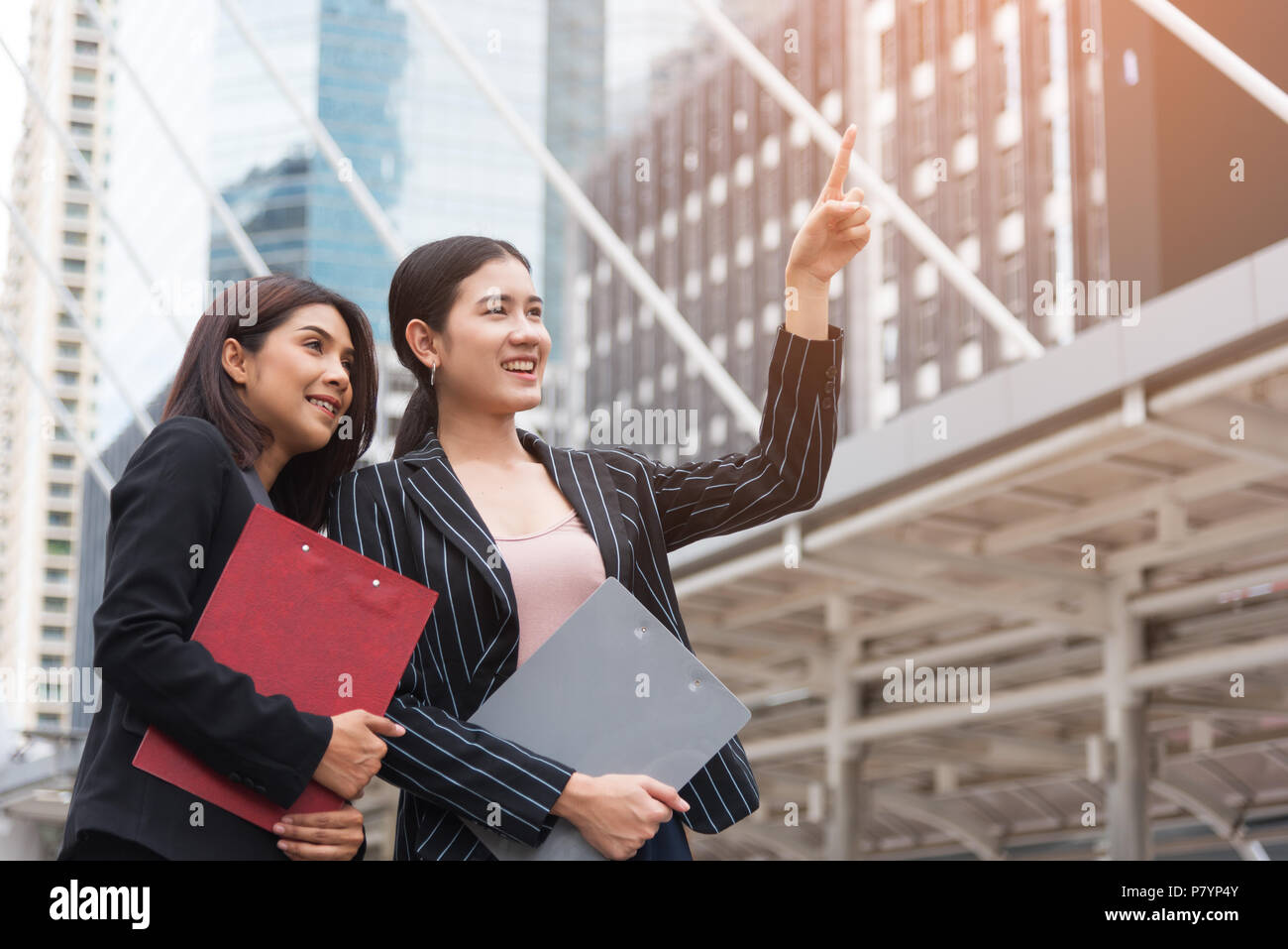 Two young beautiful business women pointing and smiling with outdoor ...