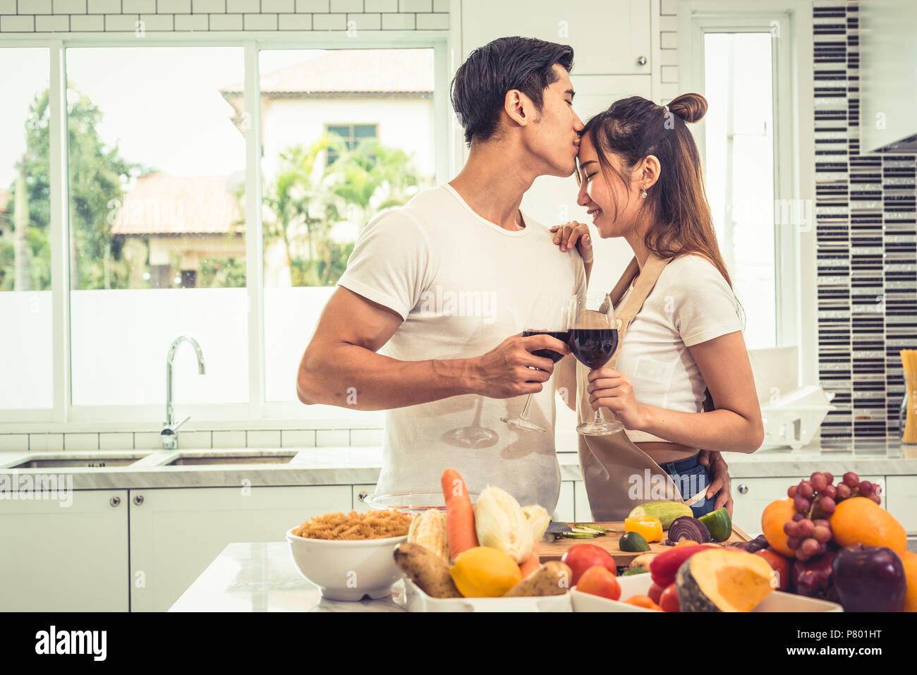 Asian lovers or couples kissing forehead and drinking wine in kitchen room at home. Love and happiness concept Sweet honeymoon and Valentine day theme Stock Photo