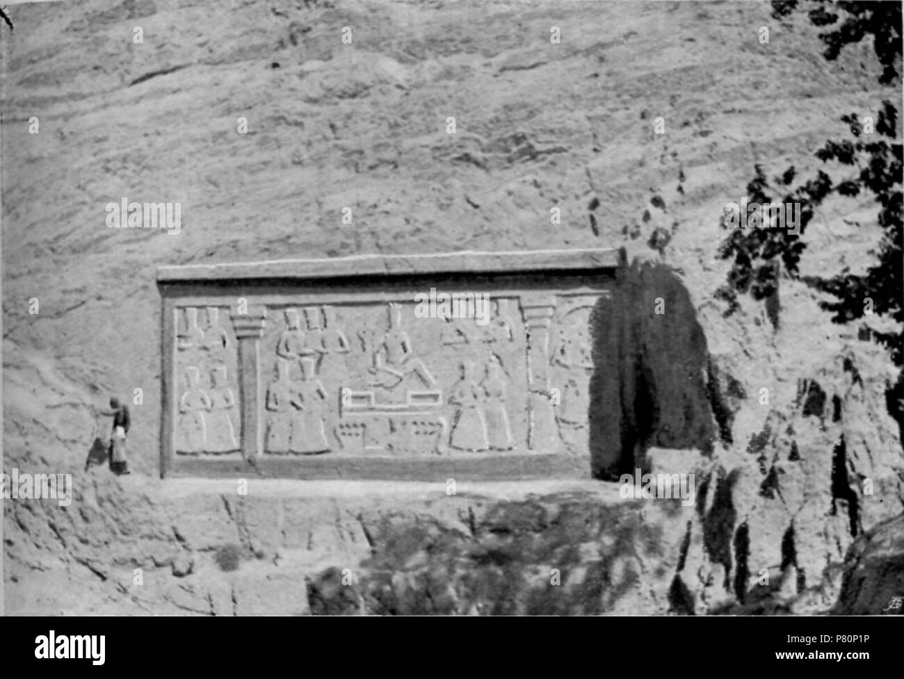 English: Rock Sculpture near Shah-Abdul-Azim. Photographed by Arnold Henry Savage Landor, 1901, probably October. From page 244 of ACROSS COVETED LANDS. Landor's description: “To the right of the road, some little distance before reaching the mosque, a very quaint, large high-relief has been sculptured on the face of a huge rock and is reflected upside down in a pond of water at its foot. Men were bathing here in long red or blue drawers, and hundreds of donkeys were conveying veiled women to this spot. An enormous tree casts its shadow over the pool of water in the forenoon. It is interesting Stock Photo