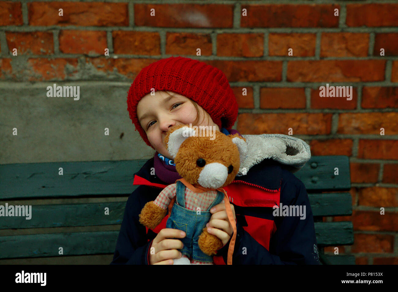 girl in red cap with teddy bear sitting on wooden banch Stock Photo