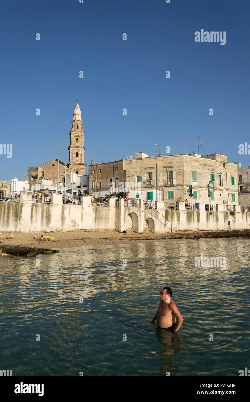 MONOPOLI, ITALY - JULY 2 2018: People swimming on beach Porta Vecchia near Cathedral during sunrise on July 2, 2018 in Monopoli, Italy. Stock Photo