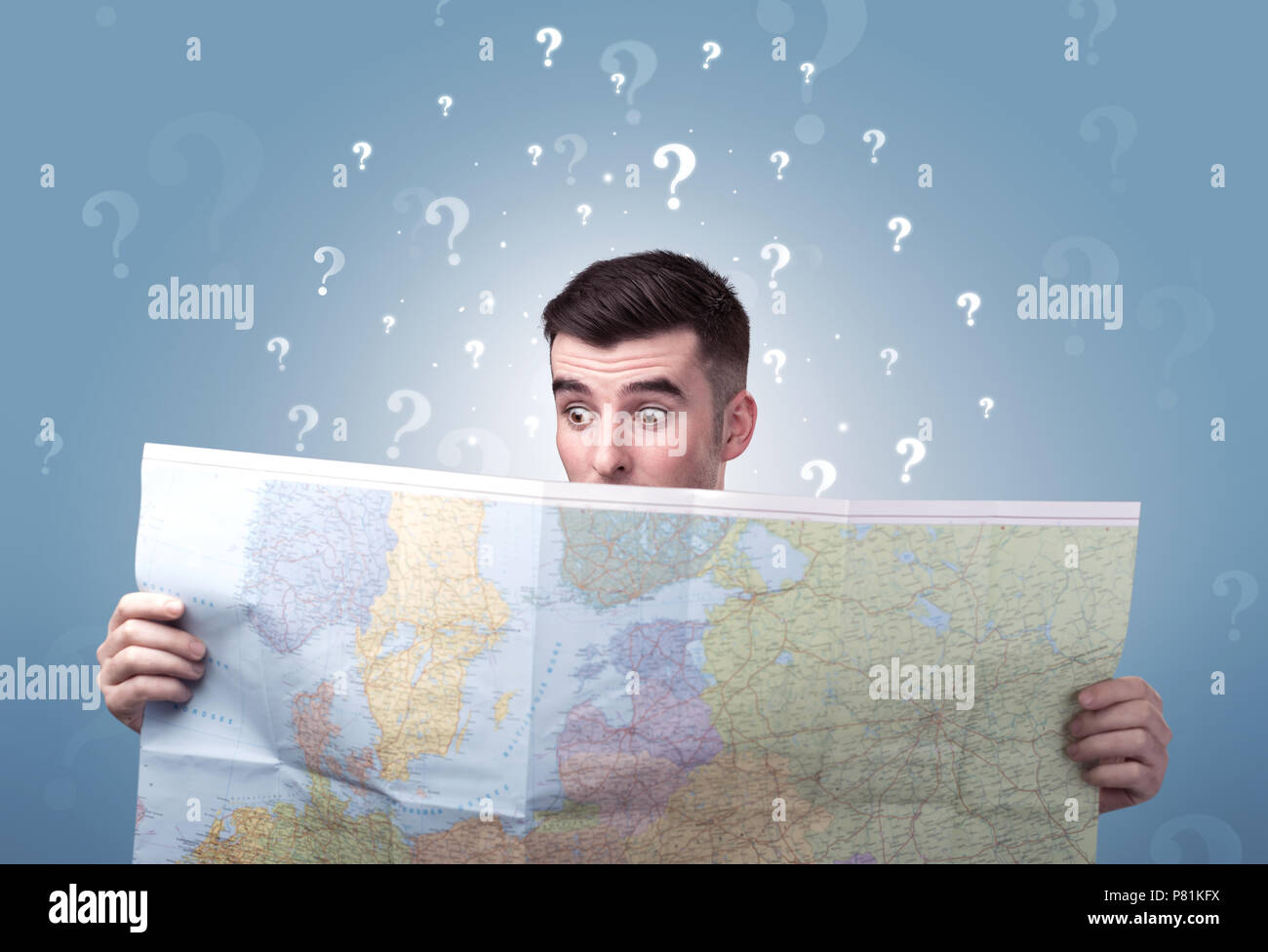 Handsome young man holding a map with white question marks above his ...