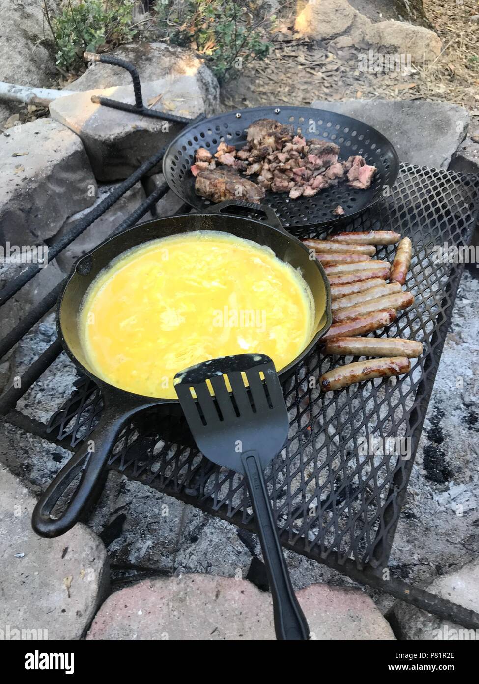 Cooking sausages in cast iron skillet on campfire while camping. Good and  positive campfire food. Stock Photo