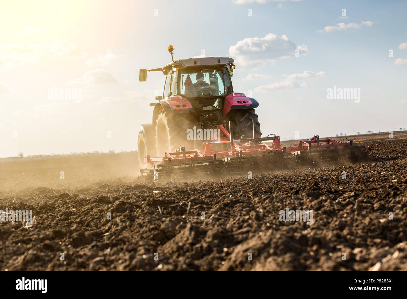 Farmer in tractor preparing land with seedbed cultivator as part of pre seeding activities in early spring season of agricultural works at farmlands. Stock Photo