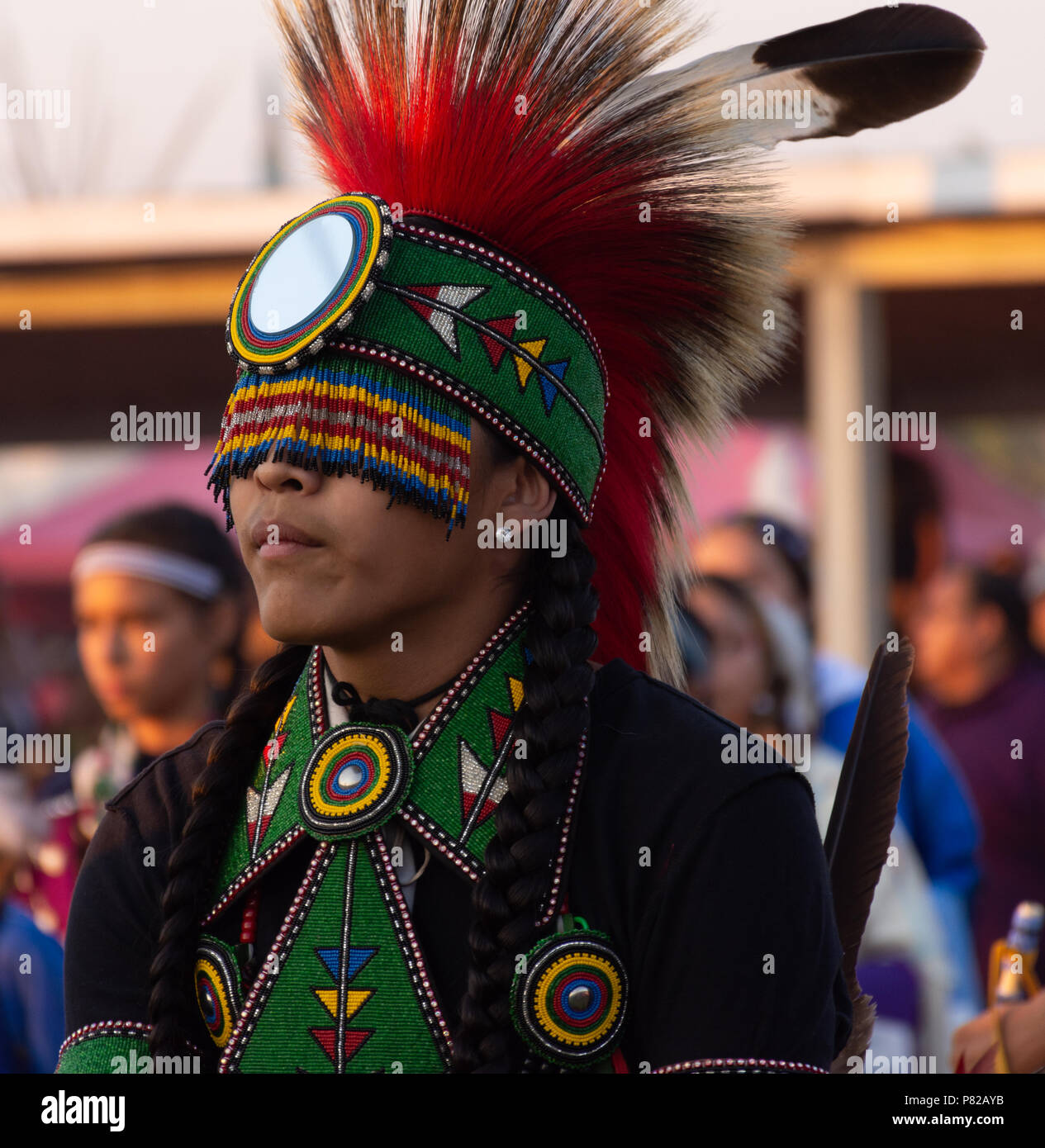 A young Native American male pow wow dancer with a beaded headband and  adornments to costume. His black hair is braided and his eyes are shielded by  Stock Photo