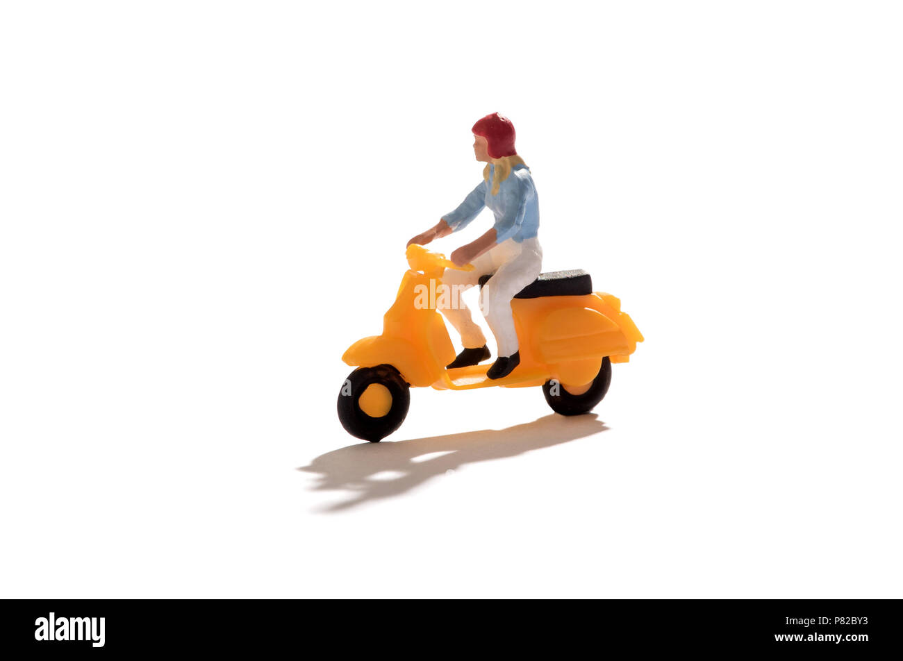 Miniature person riding a bright yellow scooter isolated on white with copy space with a front shadow Stock Photo