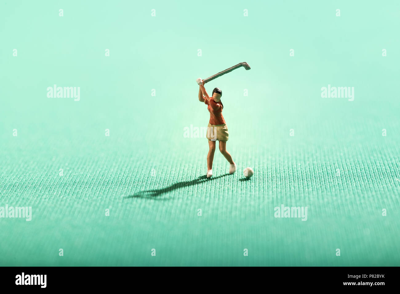 Miniature woman playing golf on a green swinging her golf club or driver as she plays a shot with shadow and copy space Stock Photo