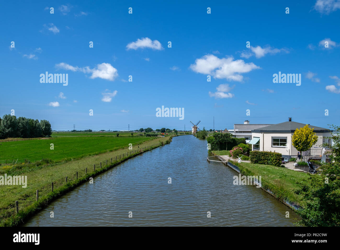 Typical Dutch polder with polder canal and polder mill at the horizon. Stock Photo