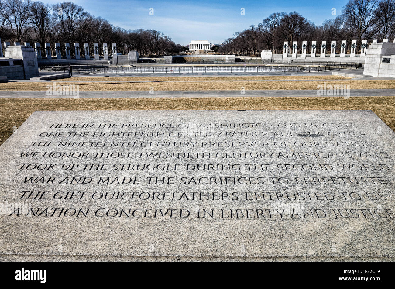 A view over the National World War II Memorial on the National Mall in Washington DC. In the foreground is a stone incription at the memorial. In the background is the Reflecting Pool and Lincoln Memorial. Stock Photo