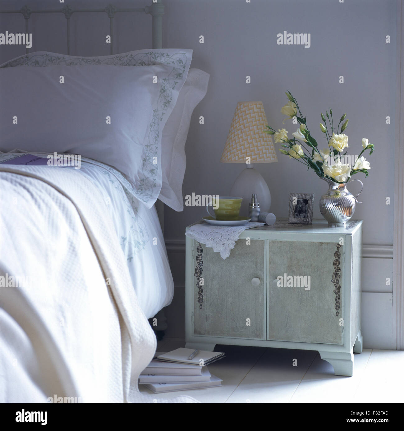 Small lamp and a jug of white roses on a newly renovated and painted vintage bedside cabinet Stock Photo