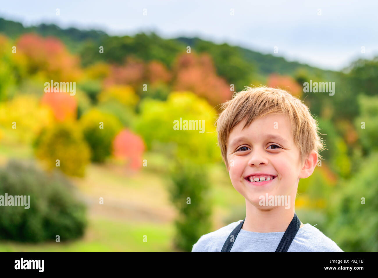 Portrait of smiling aussie boy with autumn trees on background Stock Photo