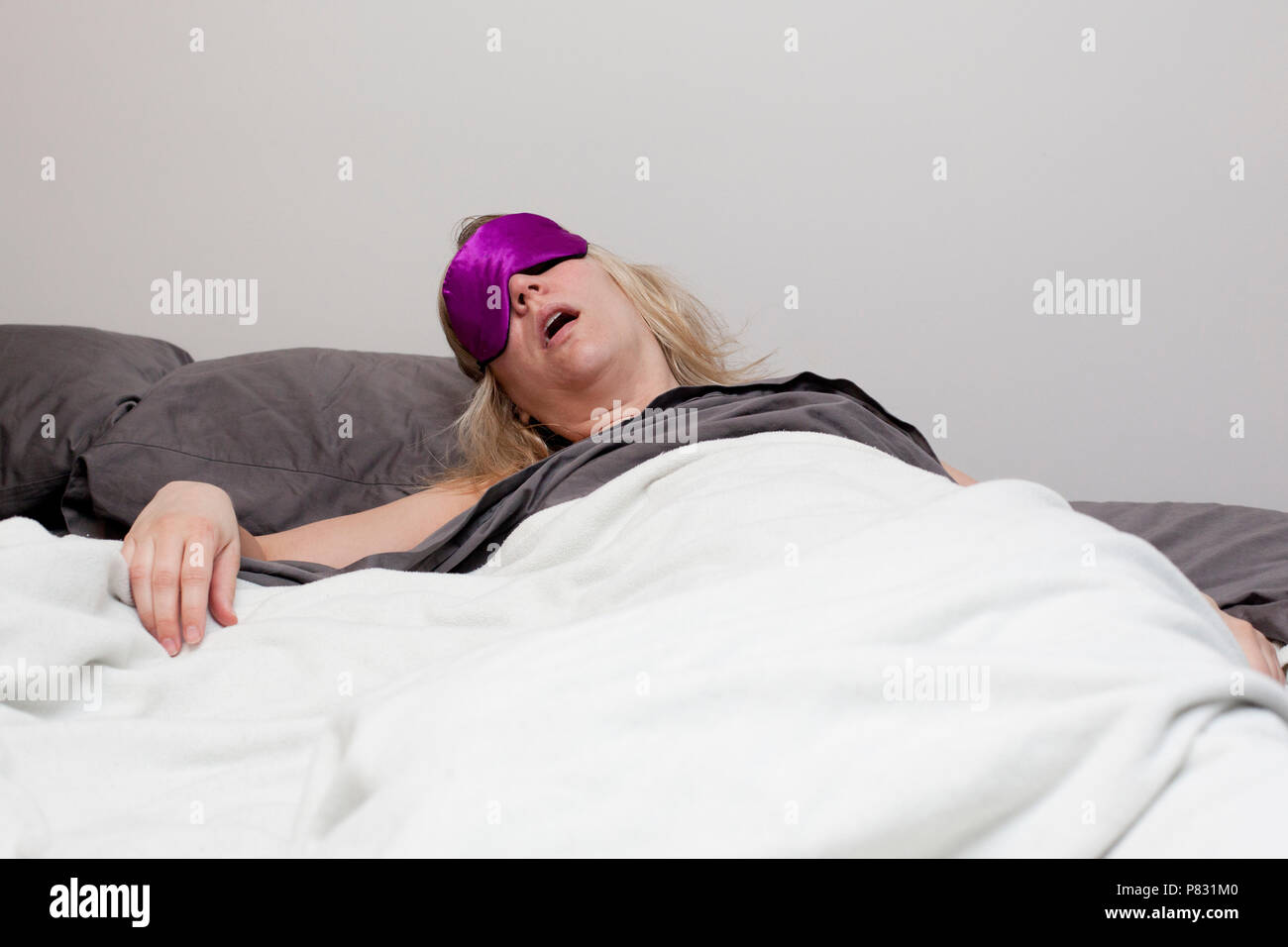 A woman wearing an eye mask is in bed confused and sleepy Stock Photo