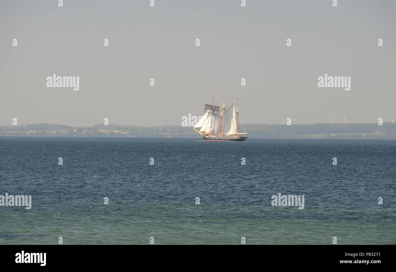 Old three masted ship with sails set, seen on distance on the sea. Stock Photo